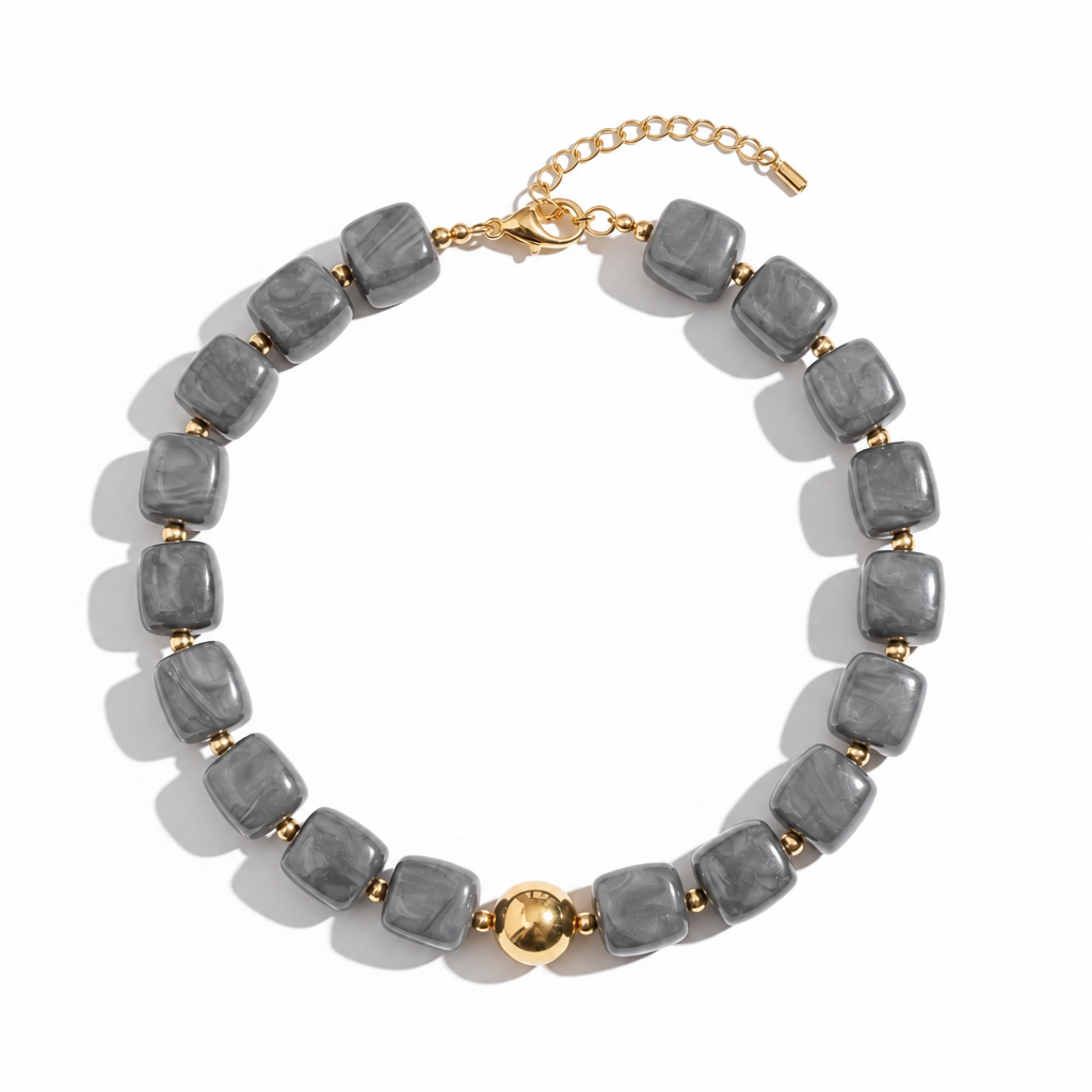 Collar de resina gris con detalles dorados sobre fondo blanco