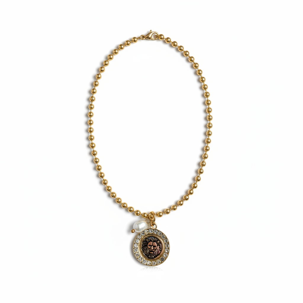 Collar dorado Roar con medallón circular de león, halo brillante y perla blanca sobre fondo blanco puro